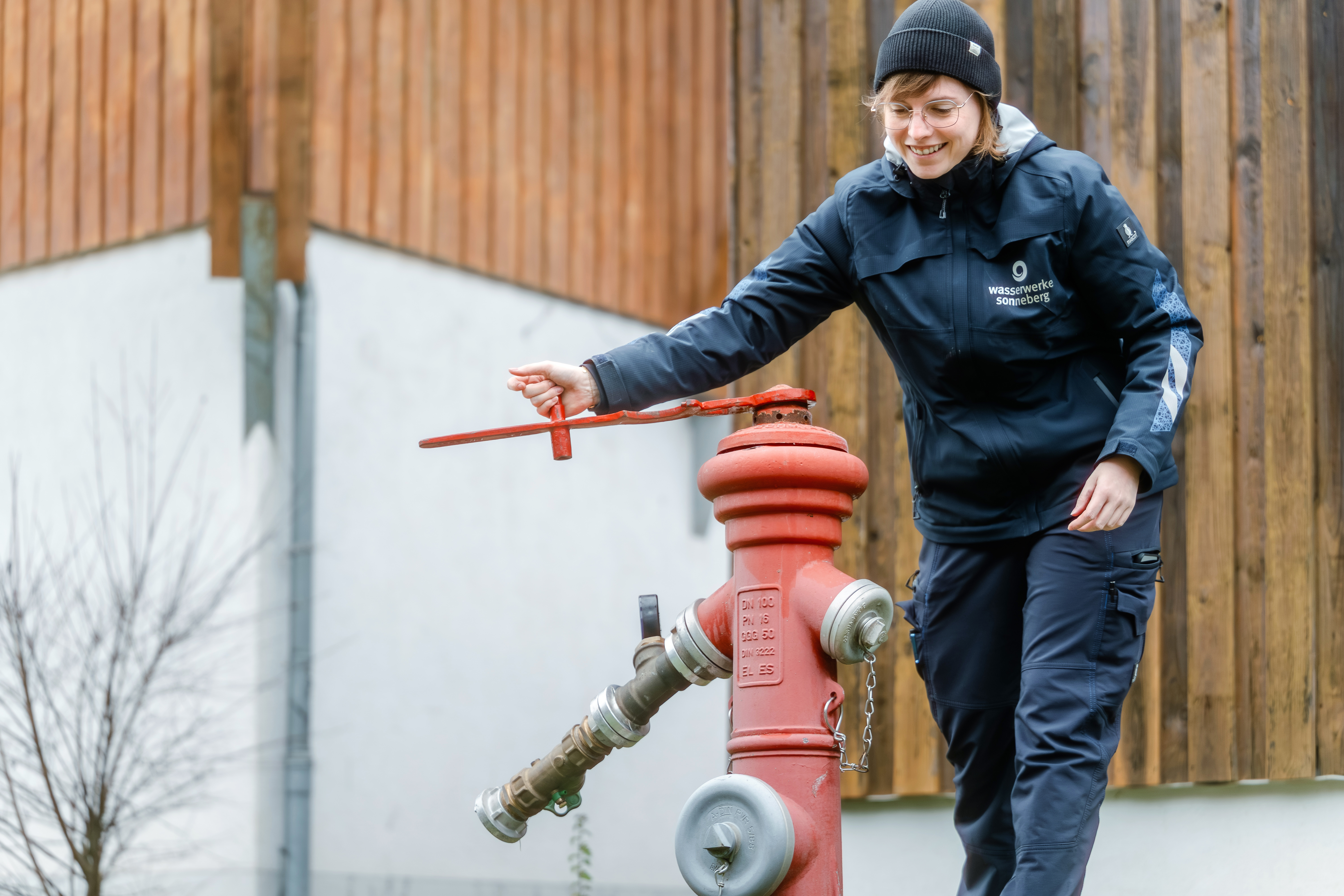 Im Bild sieht man eine Trinkwasser-Mitarbeiterin. Sie ist gerade dabei einen Hydranten zu öffnen. Sie trägt Dienstkleidung und lächelt freundlich.